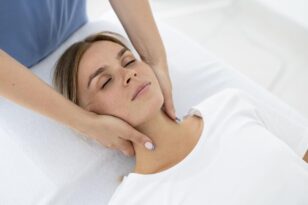 Paciente deitada em maca com quiroprata realizando segurando seu pescoço durante sessão de quiropraxia.