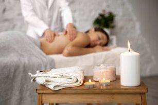 Mulher deitada recebendo uma massagem relaxante em um ambiente de spa, com velas acesas, simbolizando o bem-estar