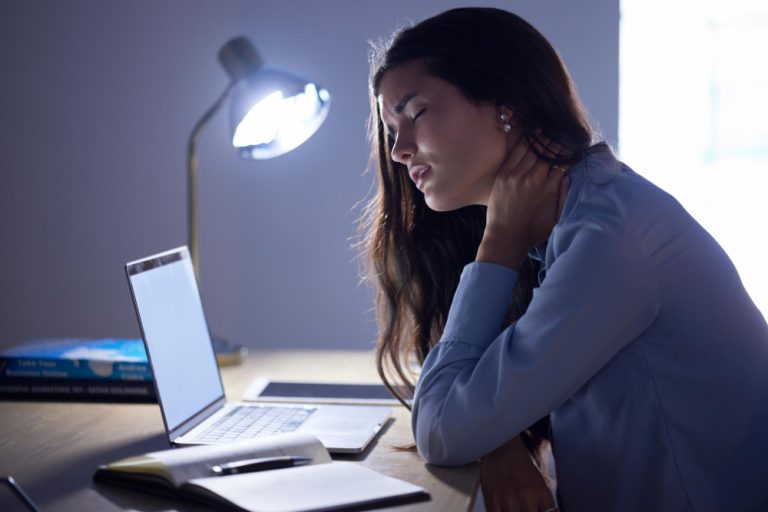 Pessoa com os ombros tensos em frente ao computador, um dos sintomas físicos de burnout mais comuns